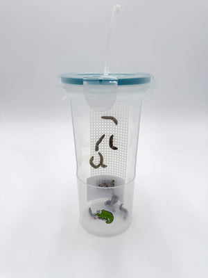 A clear plastic feeding device for chameleons with a blue lid, containing insects for feeding and a chameleon reaching out to feed.